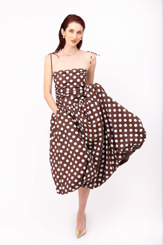 Model posing in Alexa Brown Polka Dot Puffball Dress featuring adjustable ruching, tie straps, and a full puffball midi skirt