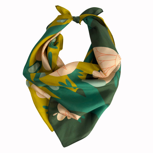 April Showers silk scarf tied in a soft bandana knot, showing green, yellow, and floral illustrated details.