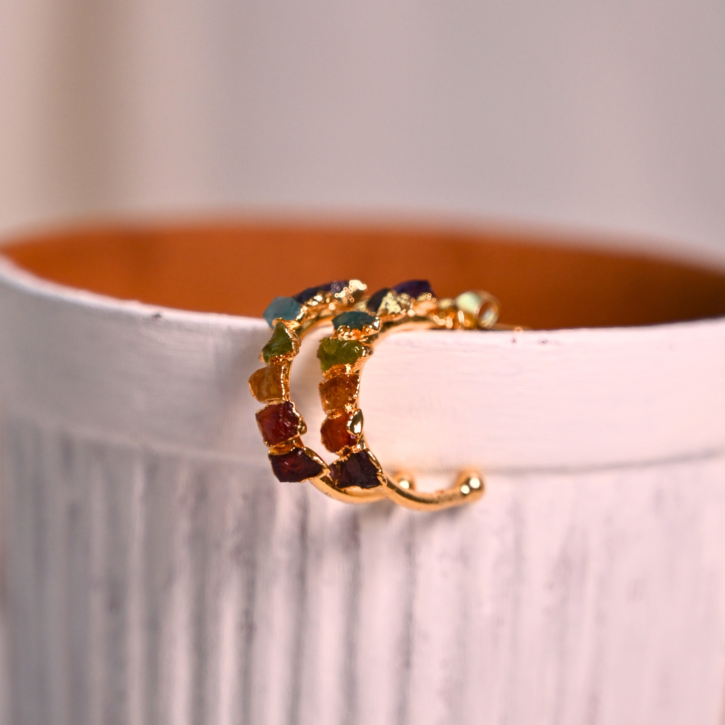Gold-plated natural stone chakra hoop earrings displayed along the edge of a ceramic vessel.