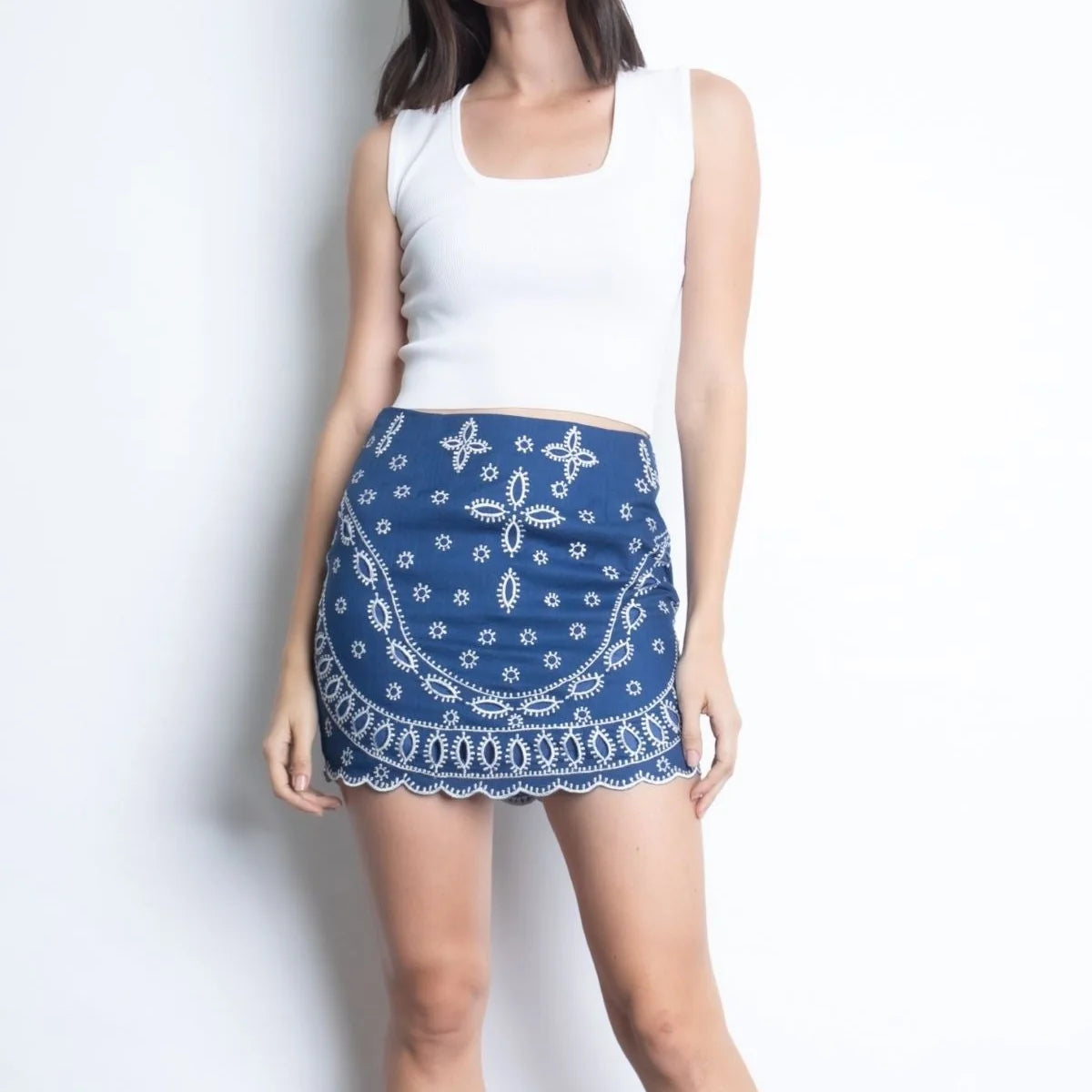 Front view of the denim-blue Illiana linen mini skirt featuring white floral embroidery and a scalloped hem.