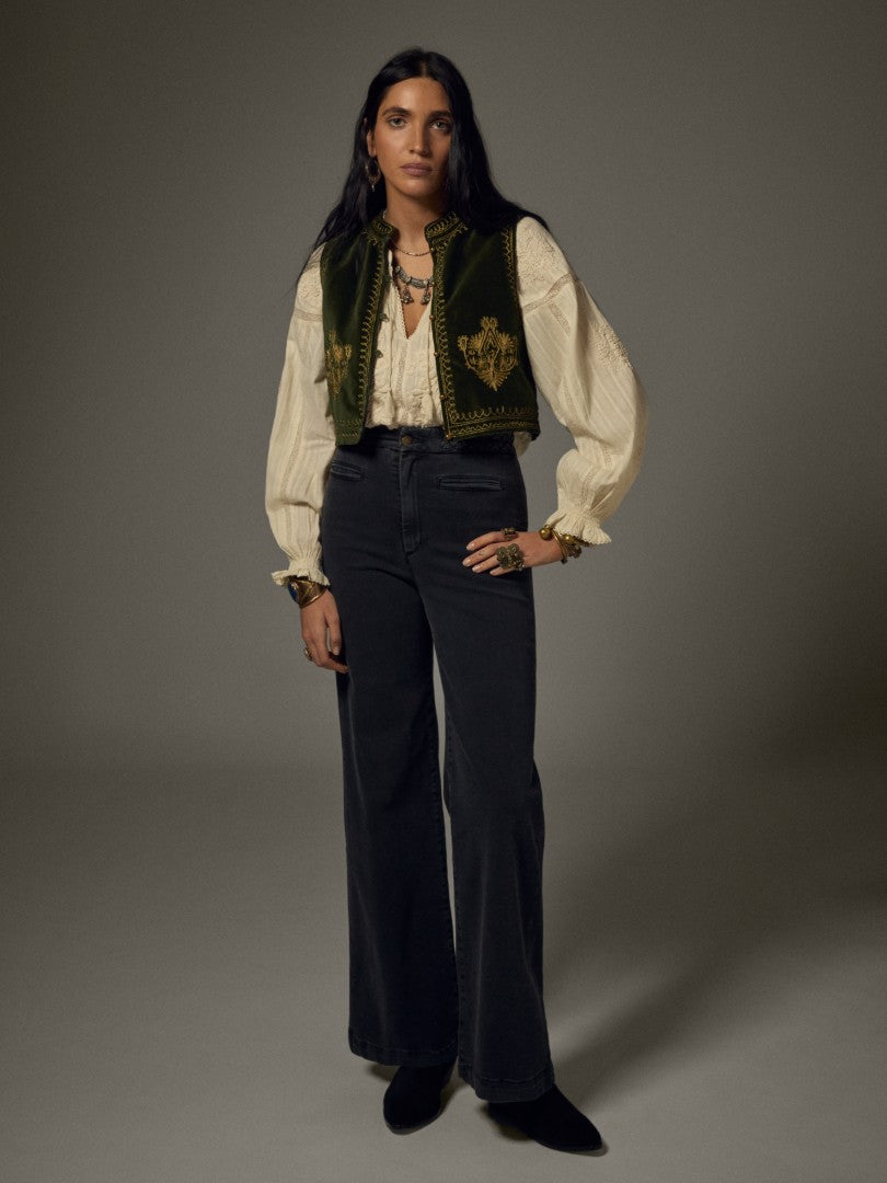 Model wearing the Maison Hotel Jimmy Vest in Hendrix Green layered over a cream blouse with dark trousers.