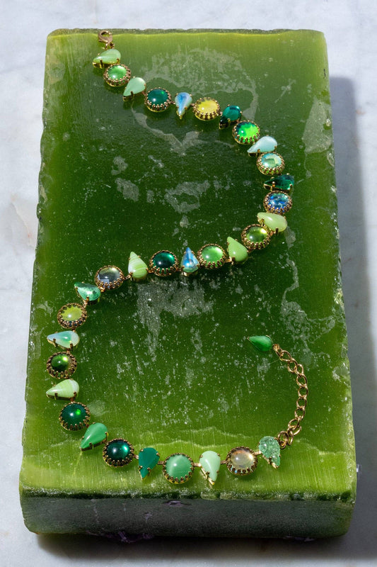 Full view of the Layering Choker in Salad Gold arranged on a green surface, featuring salad-green glass stones set in gold plate.