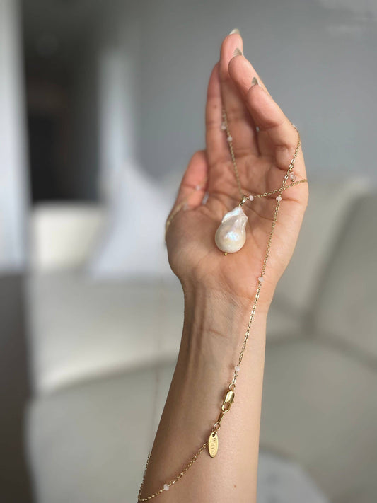 Hand holding the Long White Baroque Pearl Necklace + Herkimer Diamonds, showing the pearl pendant and gold-plated chain