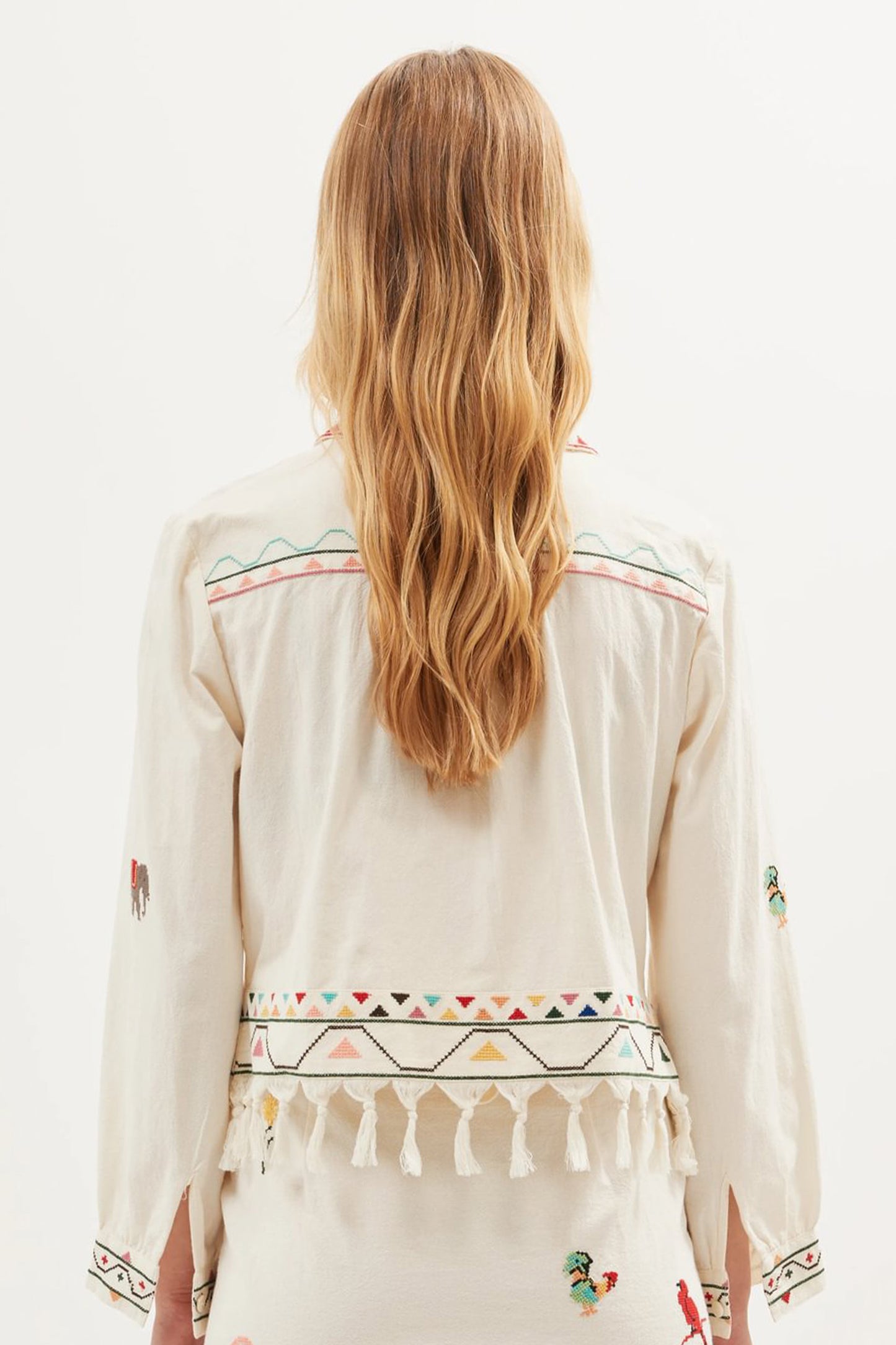 Back view of the Ludmilla Top in cream cotton with multicolor embroidered details, tassel fringe hem, and relaxed long sleeves