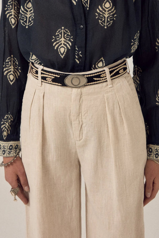 Malambo Belt styled around the waist with cream trousers and a black printed shirt, showing the black woven strap and oval gaucho-style buckle.