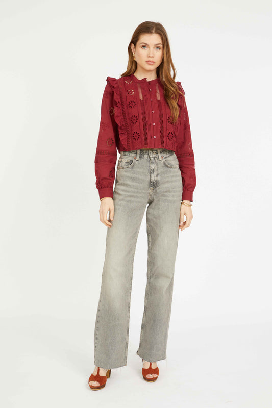 Model wearing the Nelly Top in cabernet, featuring floral eyelet embroidery, ruffle trim, mandarin collar, and cropped silhouette with light wash denim.