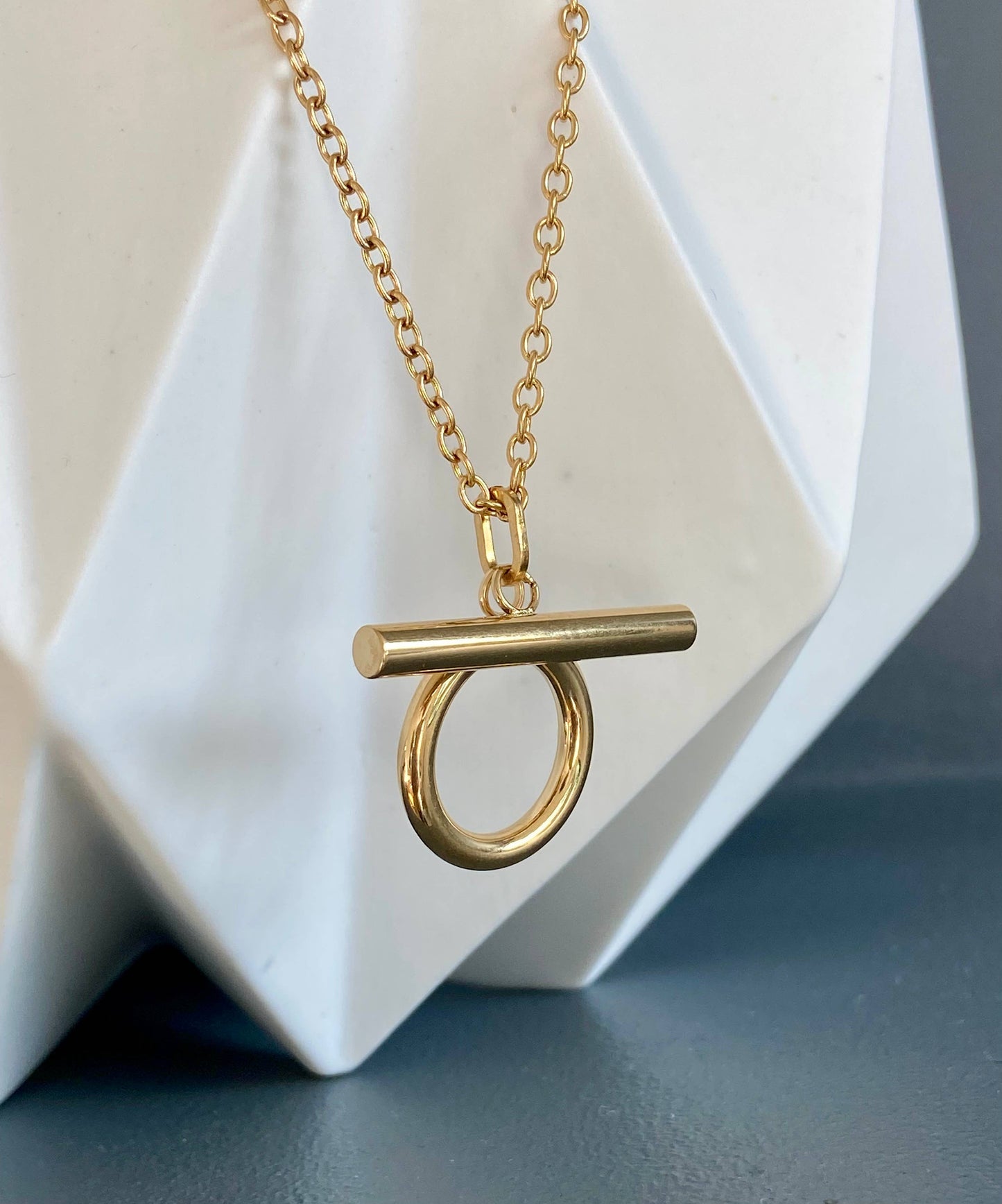 Detail view of the gold Omega Necklace and its sculptural Omega-shaped pendant on a white display.