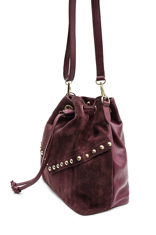 Angled view of the Régine Suede Bag in bordeaux suede showing the drawstring closure, leather trim, and stud details.