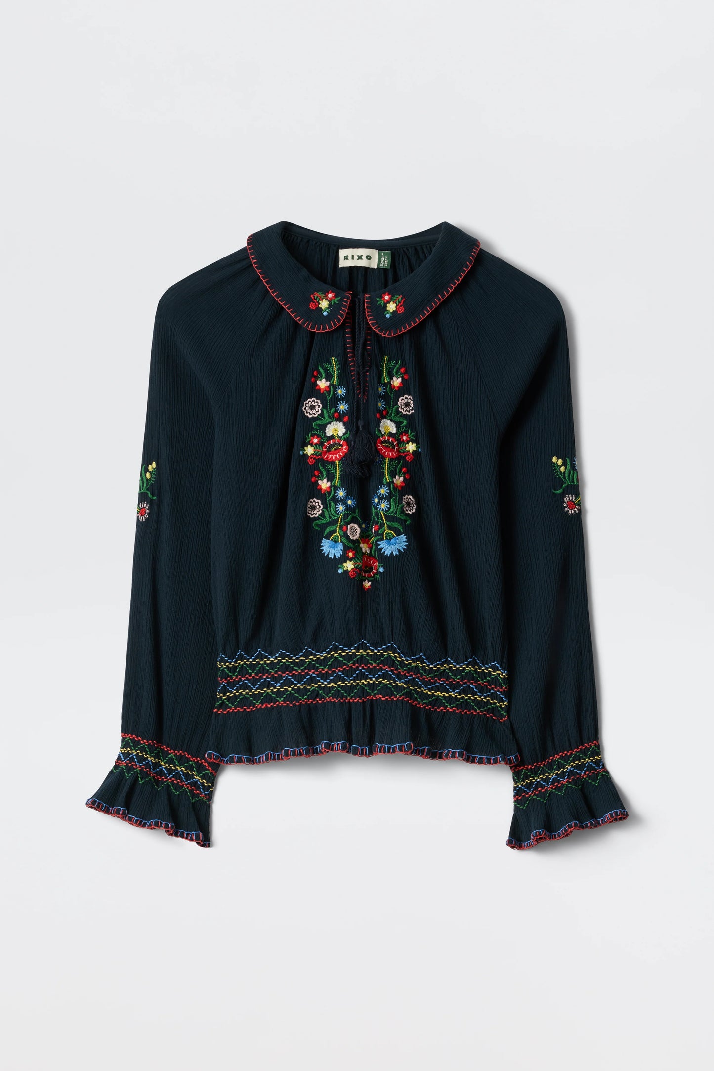 Flat lay of the navy Sofira Top with colorful floral embroidery, tie-neck detail, and ruffled cuffs