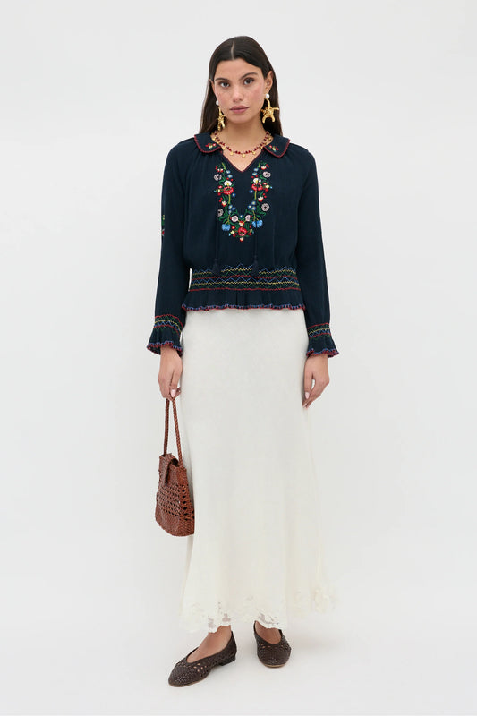 Full-length view of the Sofira Top styled with a cream skirt, featuring embroidered floral details and relaxed long sleeves