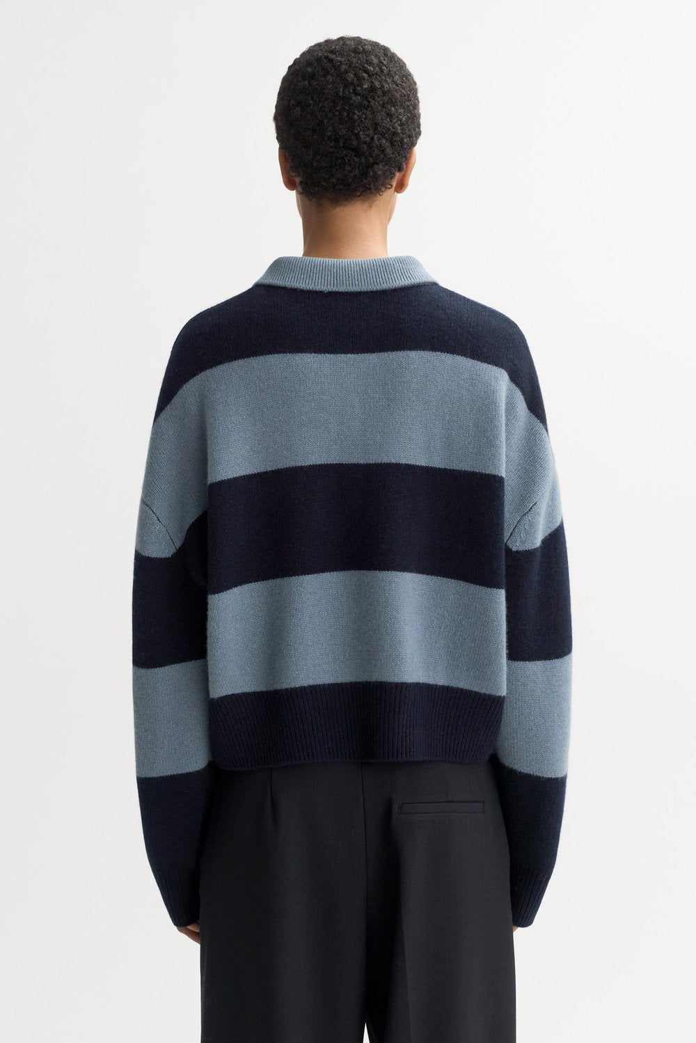 Back view of the Striped Polo Shirt in Retro Blue featuring bold navy and blue horizontal stripes, chunky cashmere knit texture, and a cropped relaxed fit.