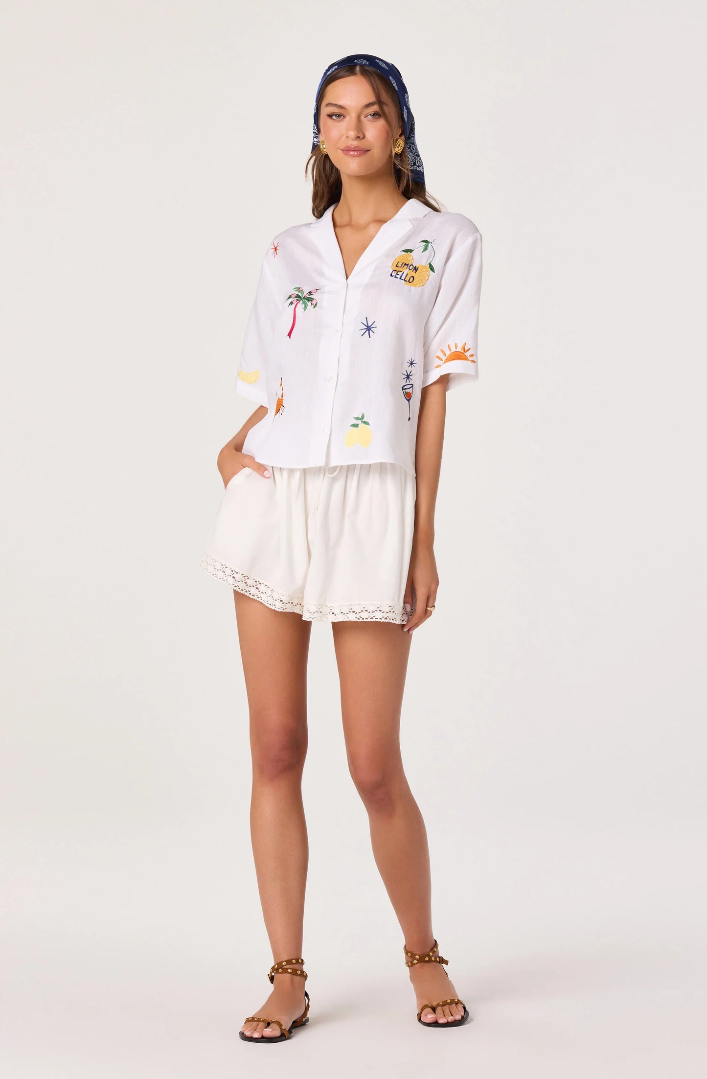 Full front view of the Vesa Embroidered Linen Button-Up Top styled with white shorts, showing the collared neckline, button-front closure, and embroidered motifs.