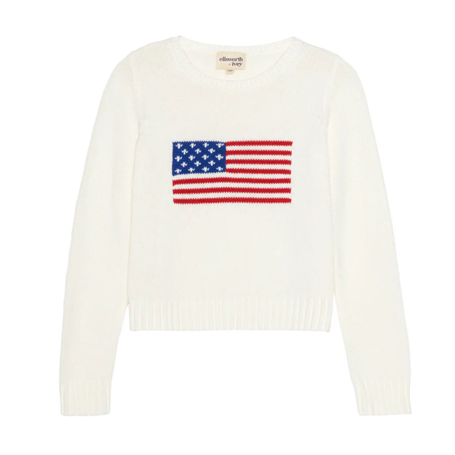 A white cropped crewneck sweater featuring a red, white, and blue American flag intarsia design across the front, with long sleeves and ribbed trim at the neckline, cuffs, and hem.