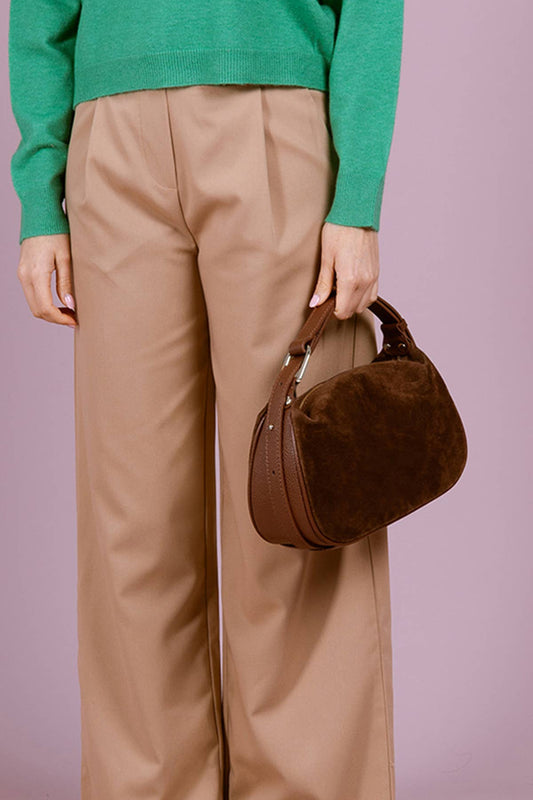 Model carrying the AMICIE Suede Bag in Khaki by hand, styled with green knitwear and neutral trousers.