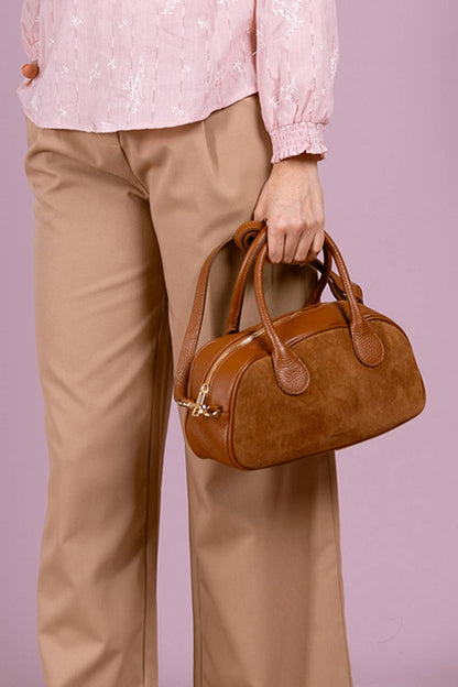 Model carrying the brown ARIELLE suede bag by its leather top handles