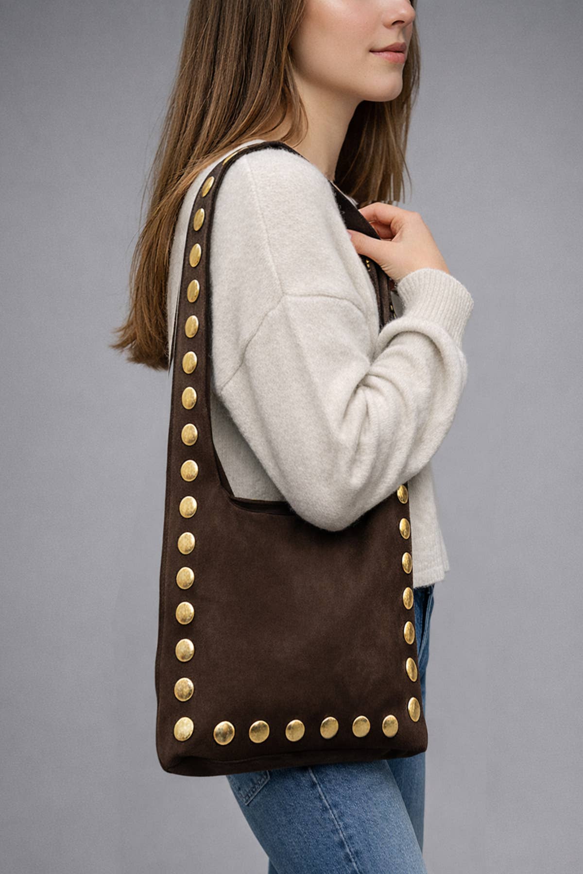 Model carrying the chocolate suede Alexane Bag over the shoulder with gold studs along the sides.