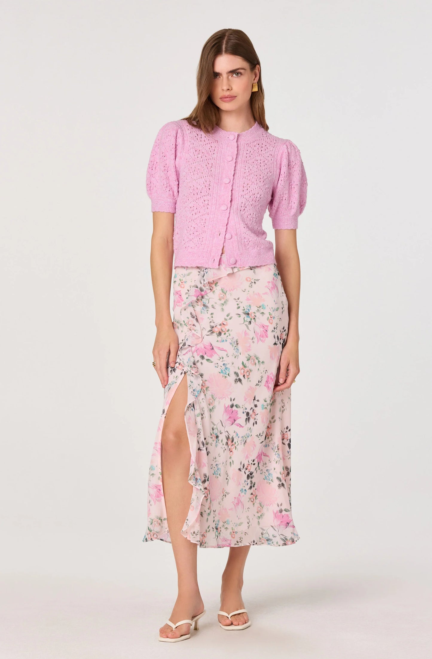 Full outfit view of the Ananda Floral Bias-Cut Ruffle Midi Skirt styled with a pink cardigan, showing the midi length and soft floral print.