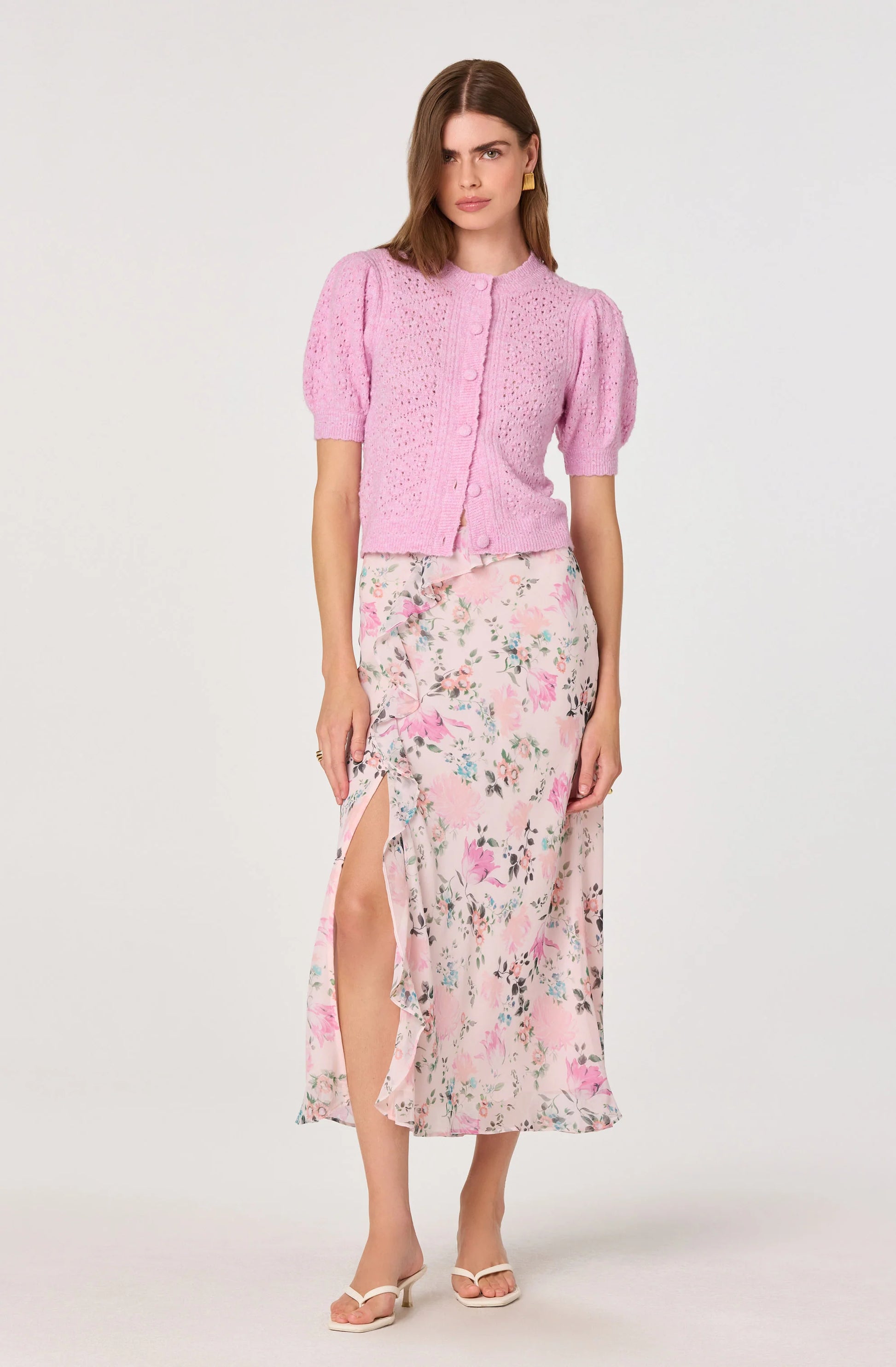 Full outfit view of the Ananda Floral Bias-Cut Ruffle Midi Skirt styled with a pink cardigan, showing the midi length and soft floral print.