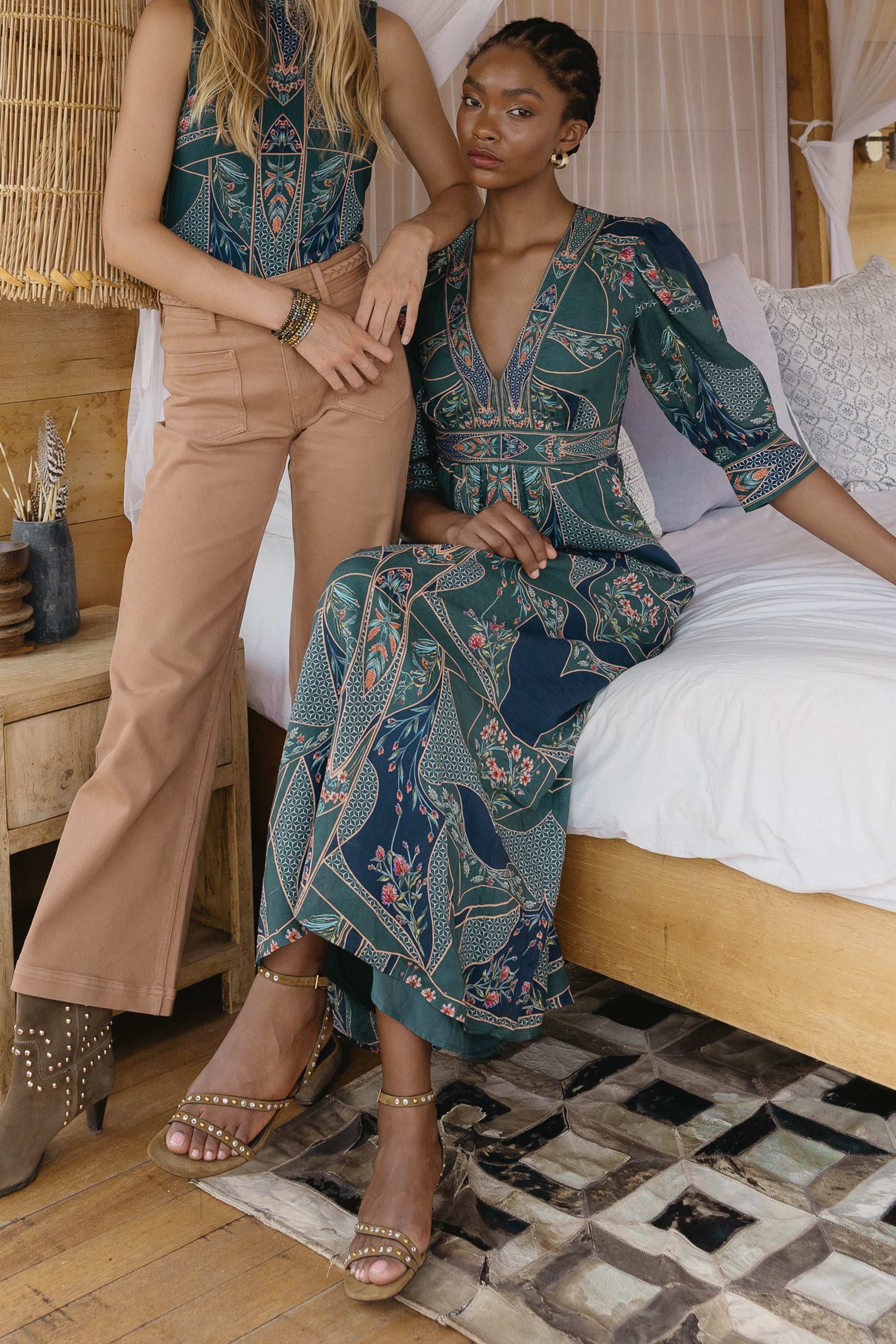 Model wearing the Aneta Dress in Patchwork Flower seated in an editorial lifestyle setting, showing the deep V-neckline and flowing maxi silhouette
