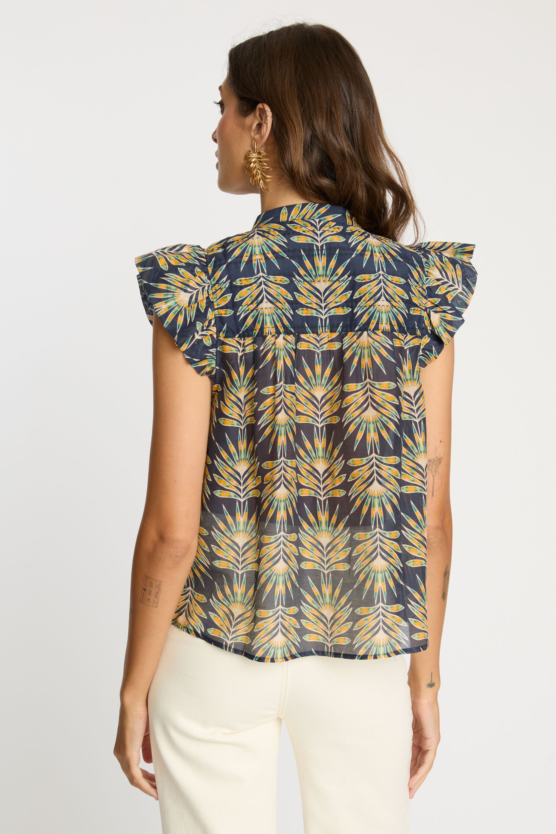 Model wearing the Anthea Top in Deco Plume featuring a dark blue tropical leaf print with flutter sleeves and a relaxed back silhouette.