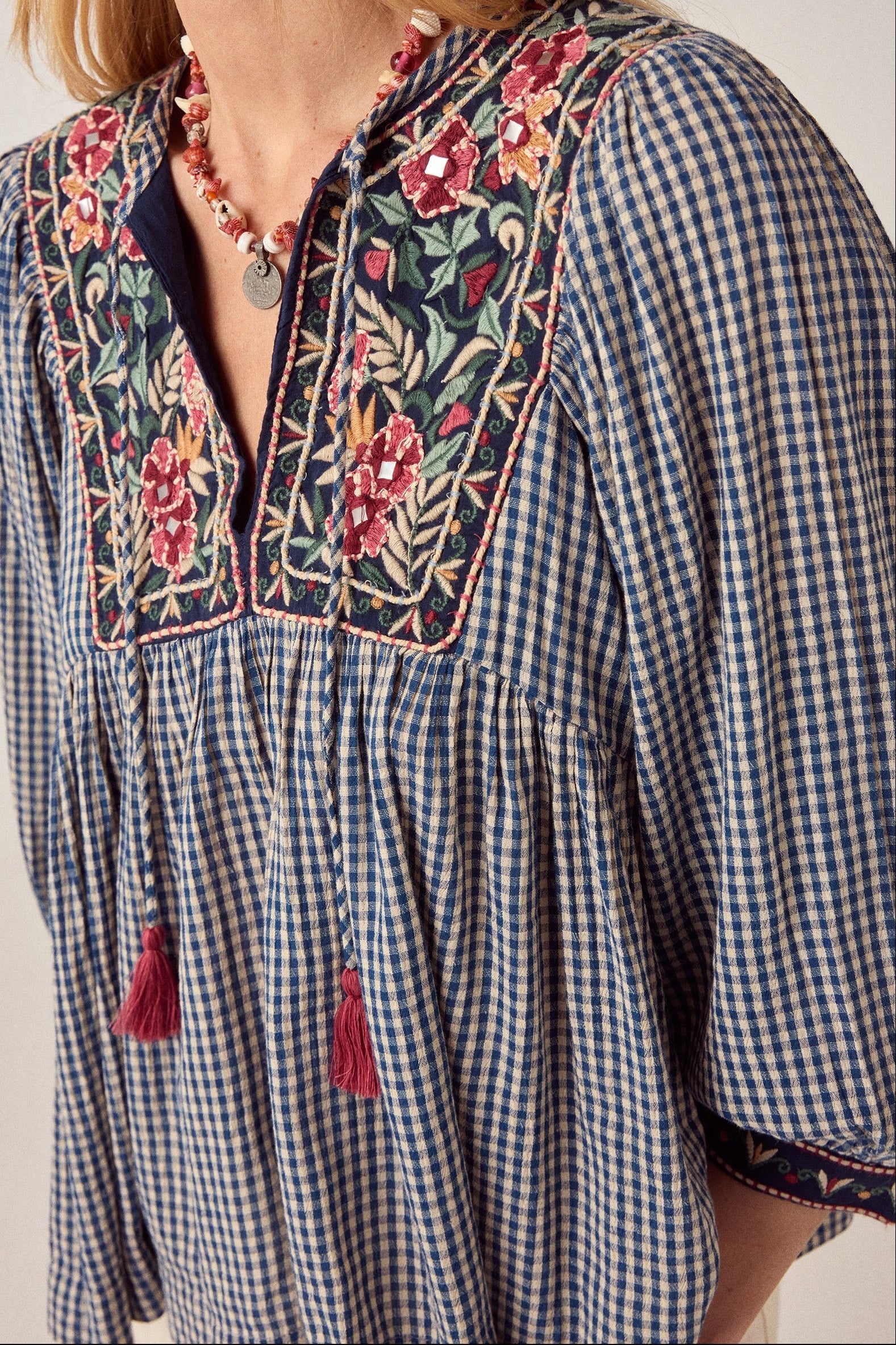Detailed close-up of the April Blouse in Bleu Picnic showing floral embroidered yoke panels, pink tassels, and soft blue gingham check pattern.