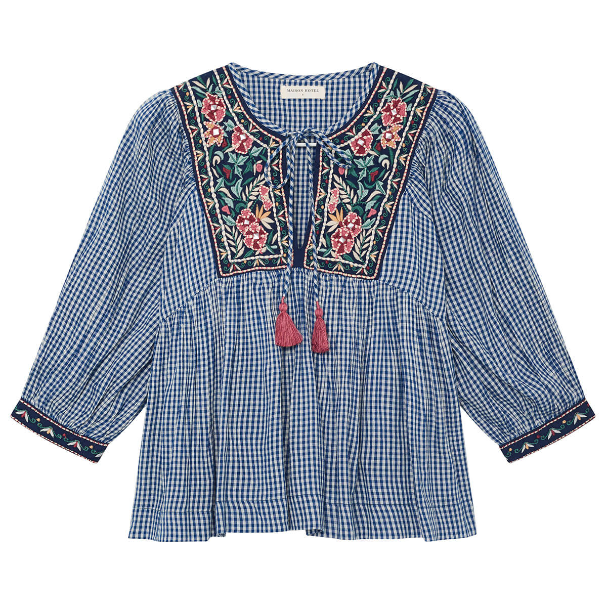 Flat lay front view of the April Blouse in Bleu Picnic featuring blue and white gingham cotton fabric, floral embroidered yoke, split V-neck with pink tassel ties, and embroidered cuffs.