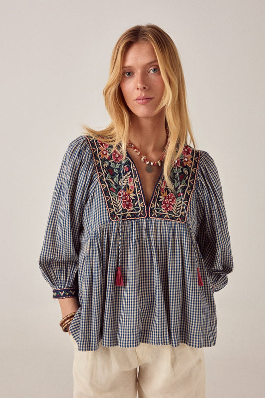 Front view of the April Blouse in Bleu Picnic featuring blue gingham check crepe fabric, floral embroidery on the yoke, split V-neckline, and pink tassel tie details.