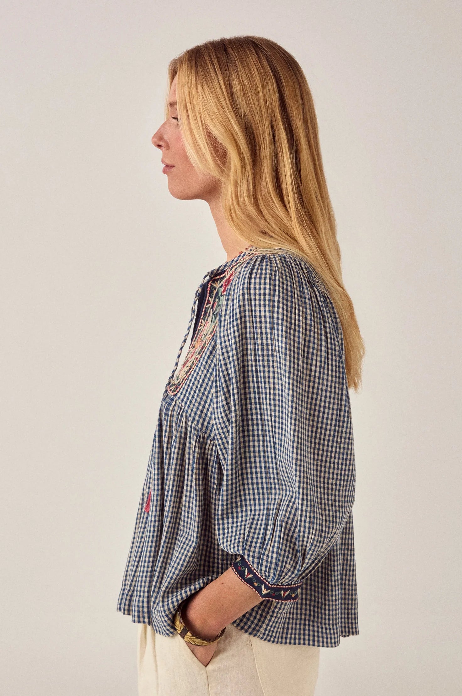 Side profile of the April Blouse in Bleu Picnic featuring a relaxed babydoll silhouette, gathered waist, embroidered cuffs, and airy gingham cotton fabric.