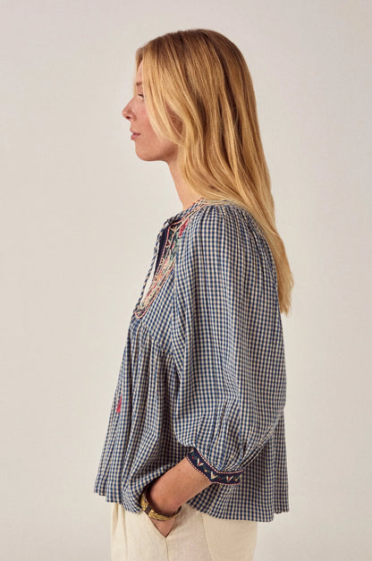 Side profile of the April Blouse in Bleu Picnic featuring a relaxed babydoll silhouette, gathered waist, embroidered cuffs, and airy gingham cotton fabric.