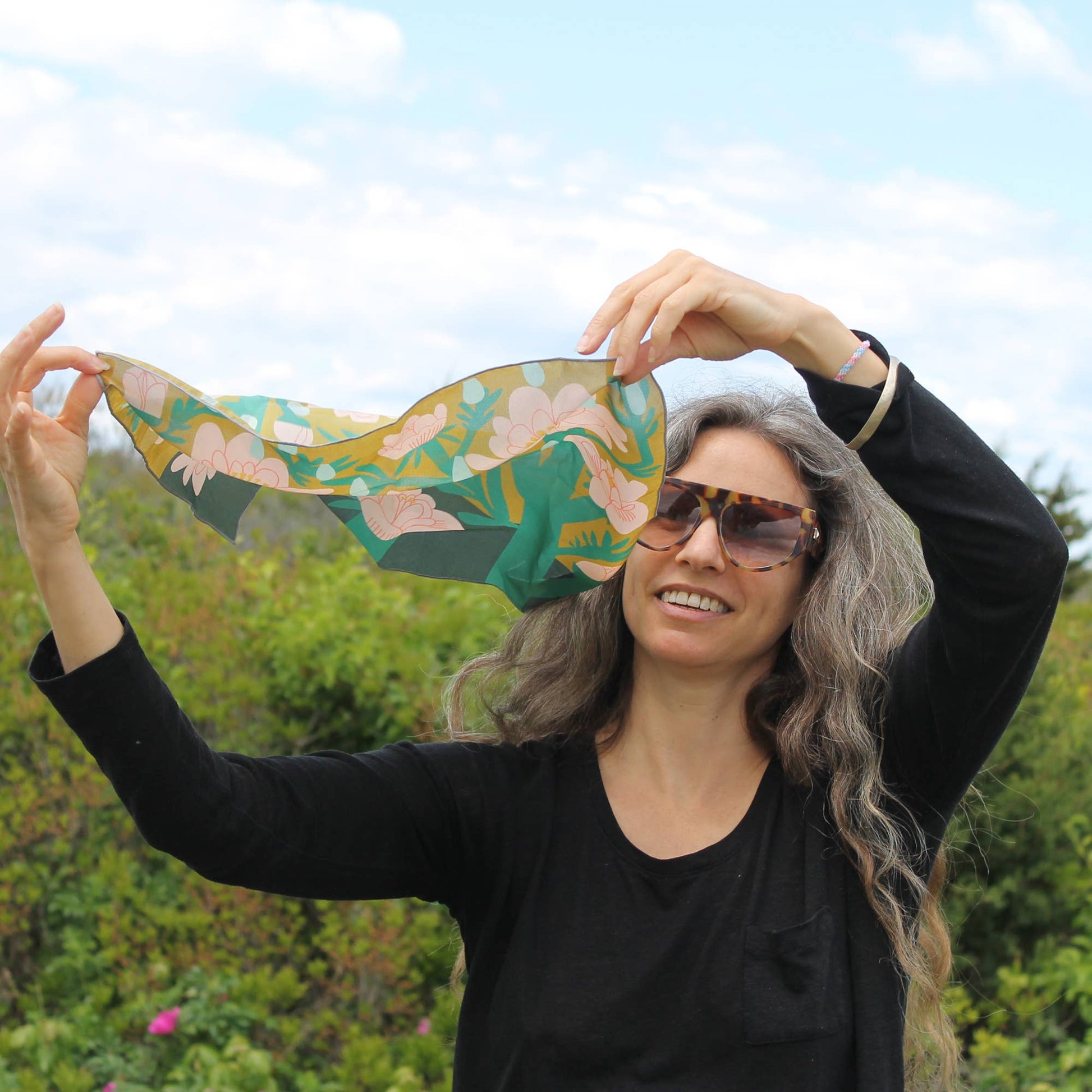 Woman styling the April Showers silk scarf outdoors, holding the floral silk square above her head.