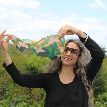 Woman styling the April Showers silk scarf outdoors, holding the floral silk square above her head.