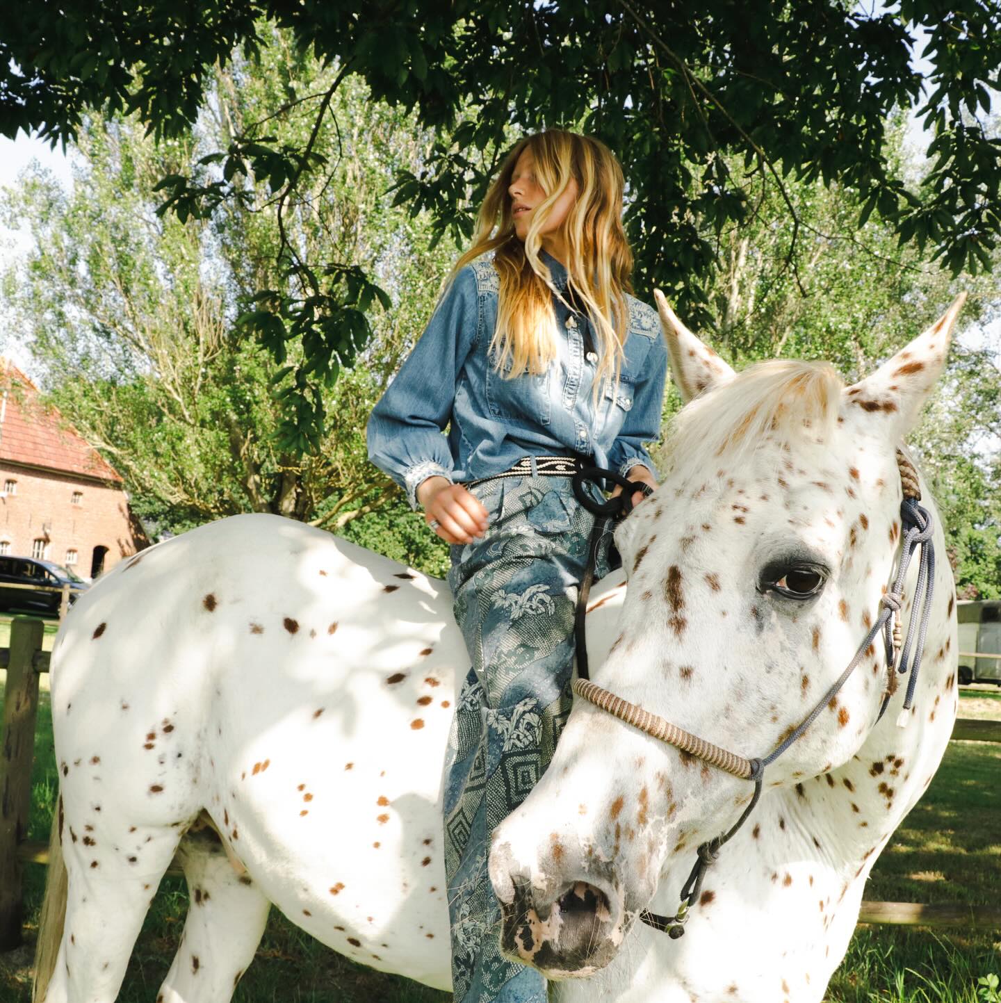 Model wearing the Arizona Thelma embroidered denim western shirt in Blue Haze while seated on a white spotted horse outdoors