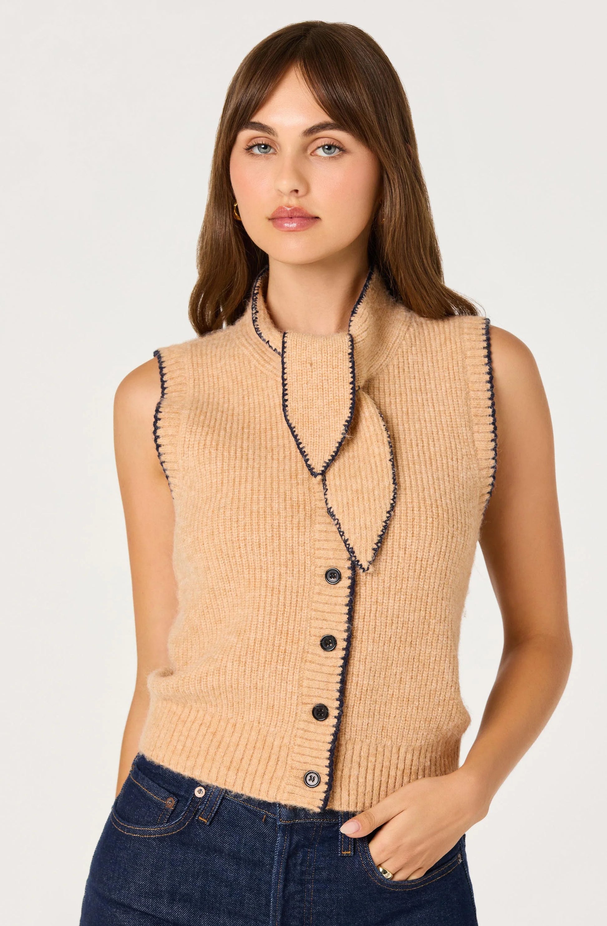 Model wearing the Auberthe Sweater Vest in beige ribbed knit with navy contrast trim, button-front closure, and cropped fit.