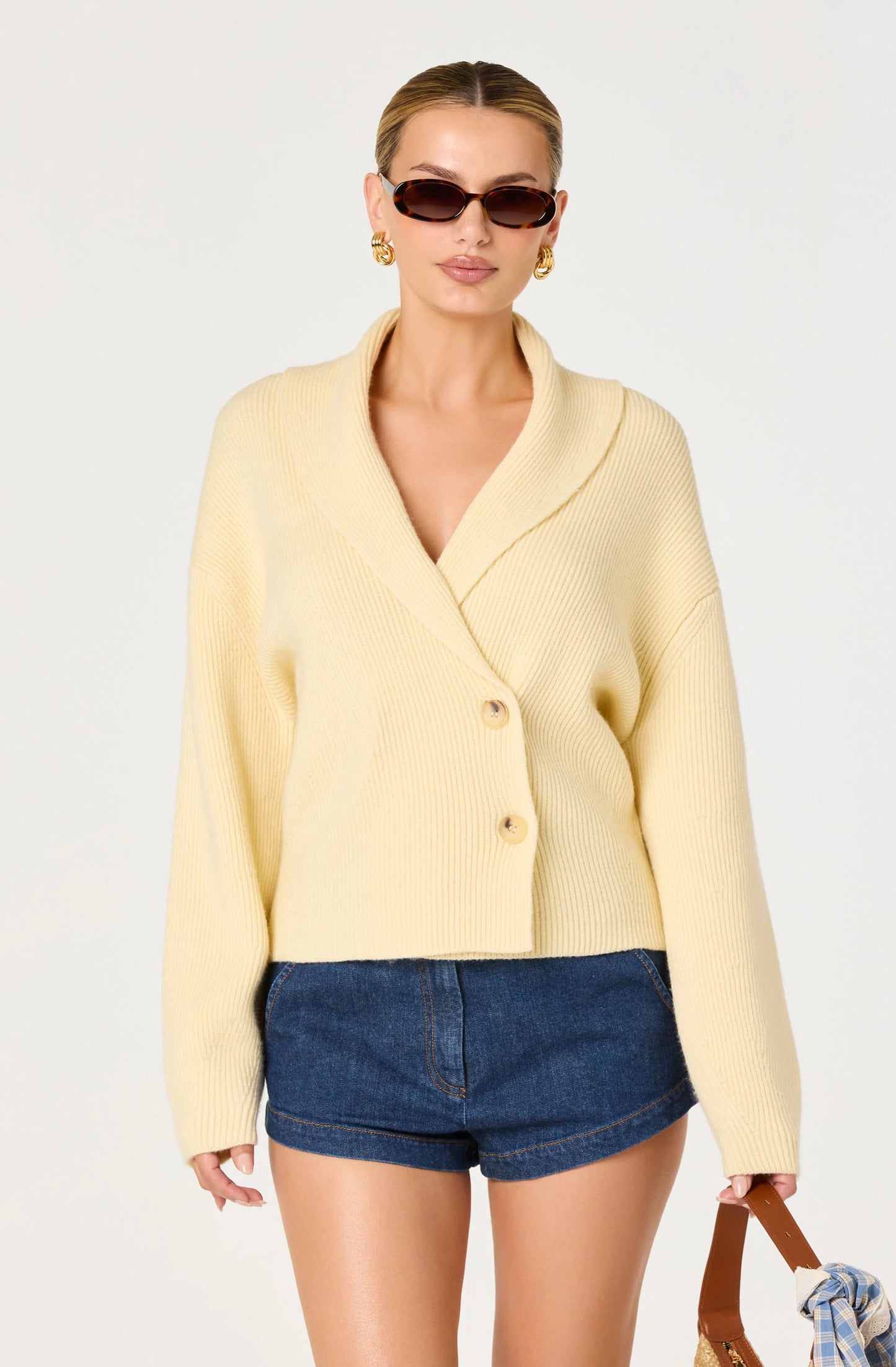 Model wearing the Ayleen Ribbed Wrap Cardigan in Butter Yellow with denim shorts, showing the wrap silhouette and relaxed long sleeves.