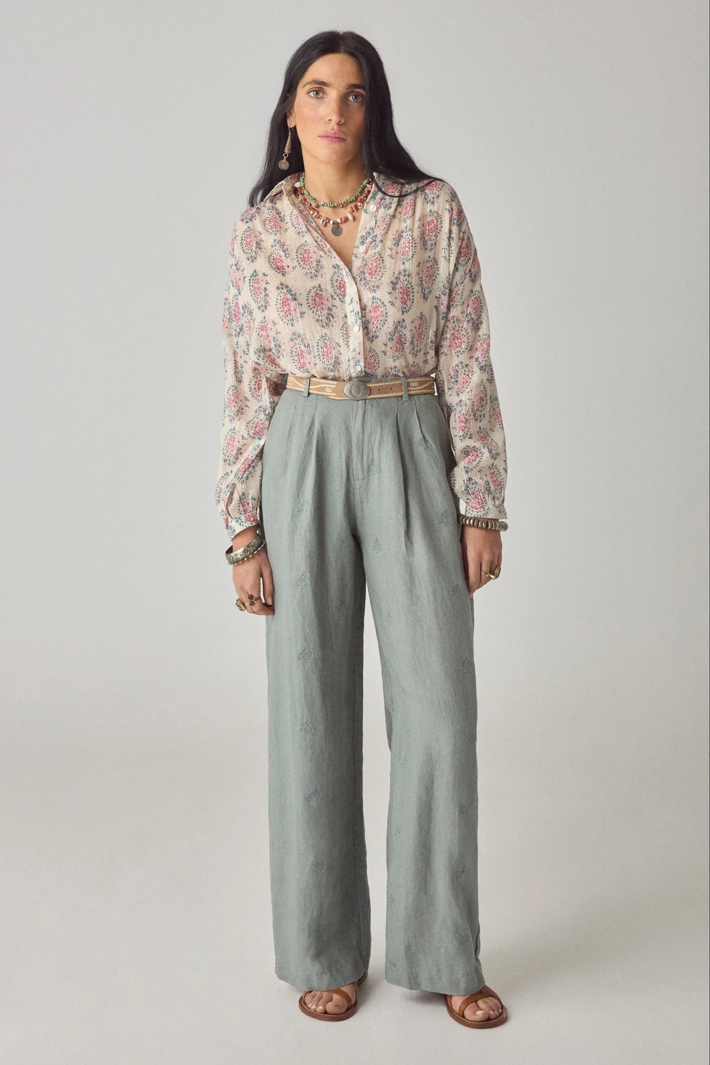Model wearing the Azalea Mary blouse in dusty cream with pink and blue floral paisley print, styled with sage wide-leg trousers and sandals.