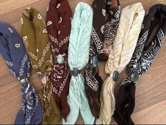 Assorted hand-distressed cotton bandanas in blue, olive, burgundy, mint, brown, cream, and black, each styled with a removable semi-precious stone slider. Crafted from 100% cotton with unique dyed and bleached patterns, showcasing the artisanal bohemian aesthetic of Stitch and Stone.