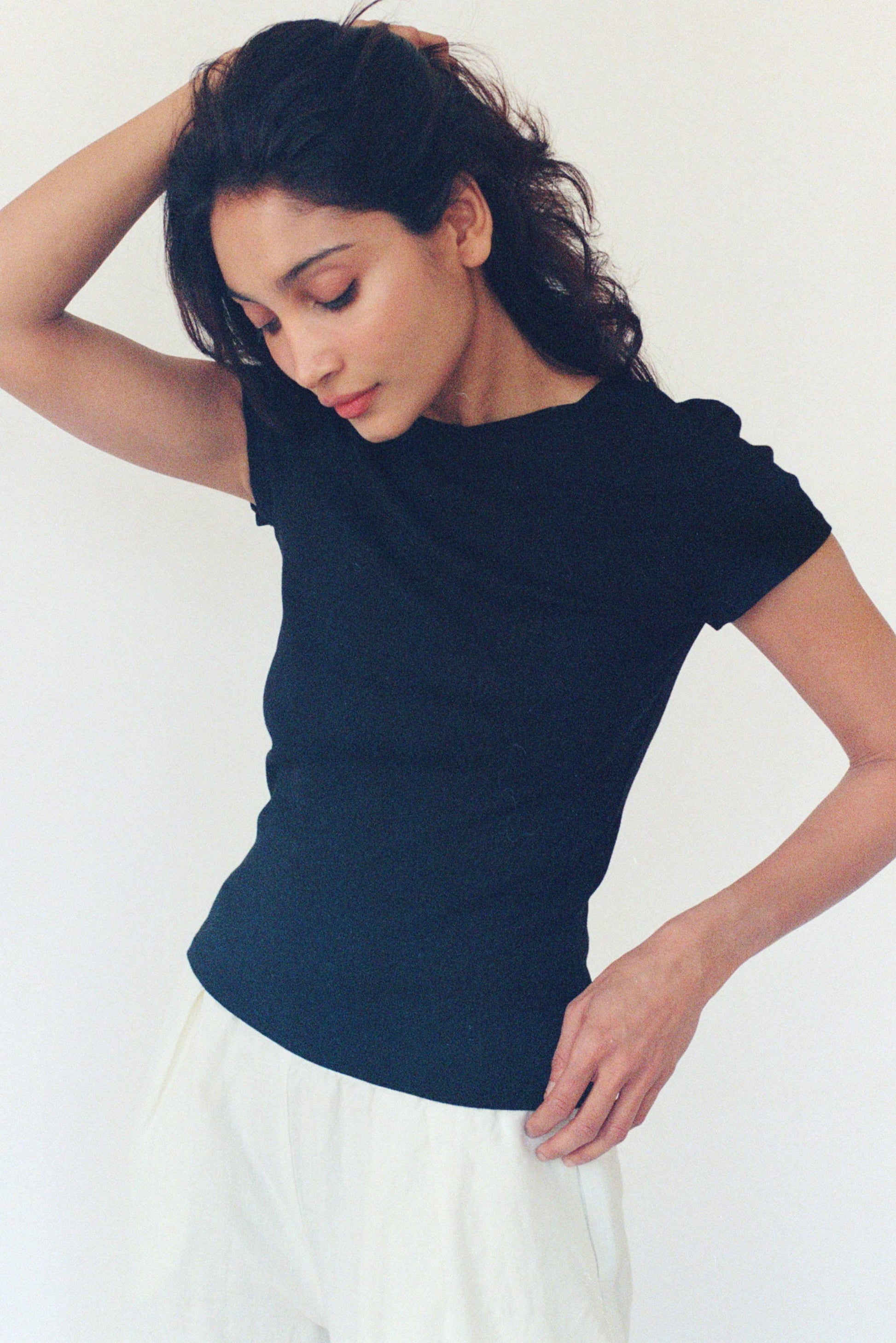 Model wearing the black Bebe Organic Tee with cap sleeves and a fitted, slightly cropped silhouette, styled with a white skirt.