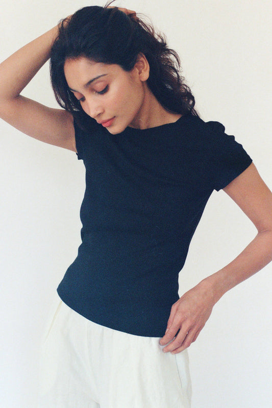 Model wearing the black Bebe Organic Tee with cap sleeves and a fitted, slightly cropped silhouette, styled with a white skirt.