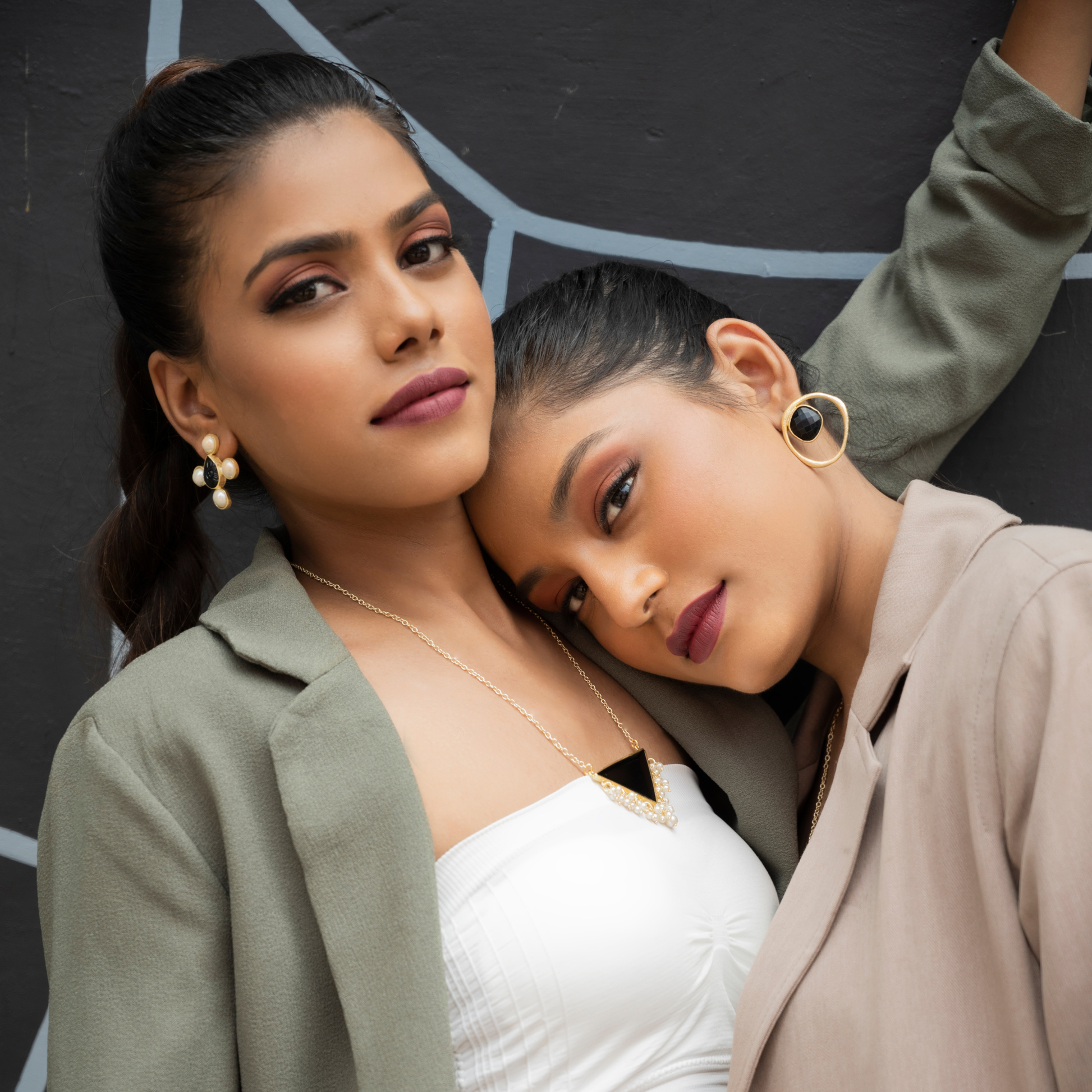 Two models wearing black onyx and gold-plated jewelry in a softly styled editorial portrait.