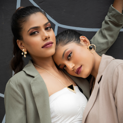 Two models wearing black onyx and gold-plated jewelry in a softly styled editorial portrait.