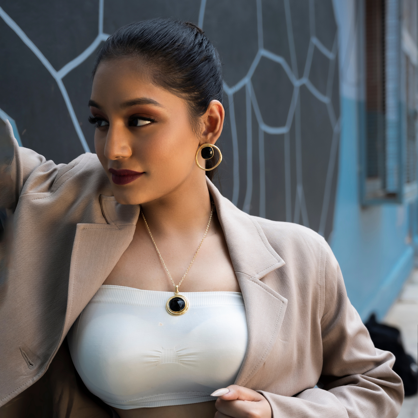 Side profile of a model wearing black onyx jewelry with a white top and taupe blazer.