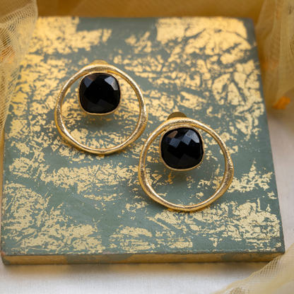 Pair of black onyx stud earrings with gold-plated circular frames arranged on a vintage decorative book.