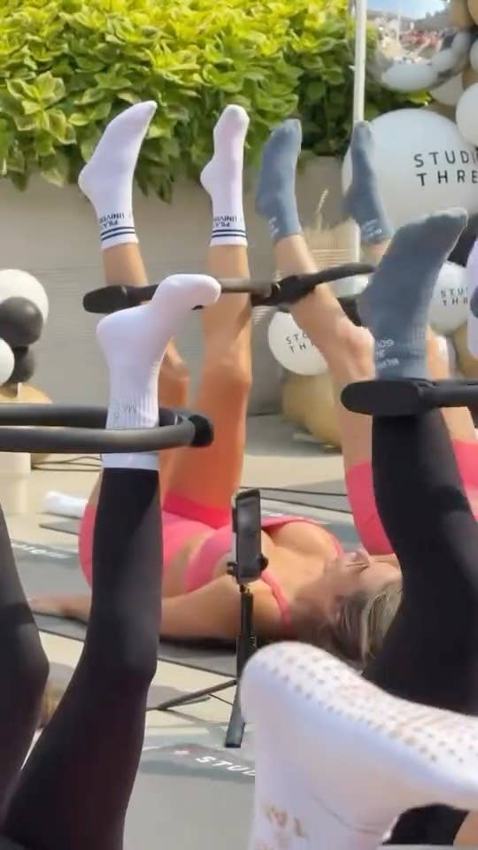 Group fitness participants wearing blue and white BURNS SO GOOD grip socks while performing leg exercises on reformer Pilates machines outdoors.