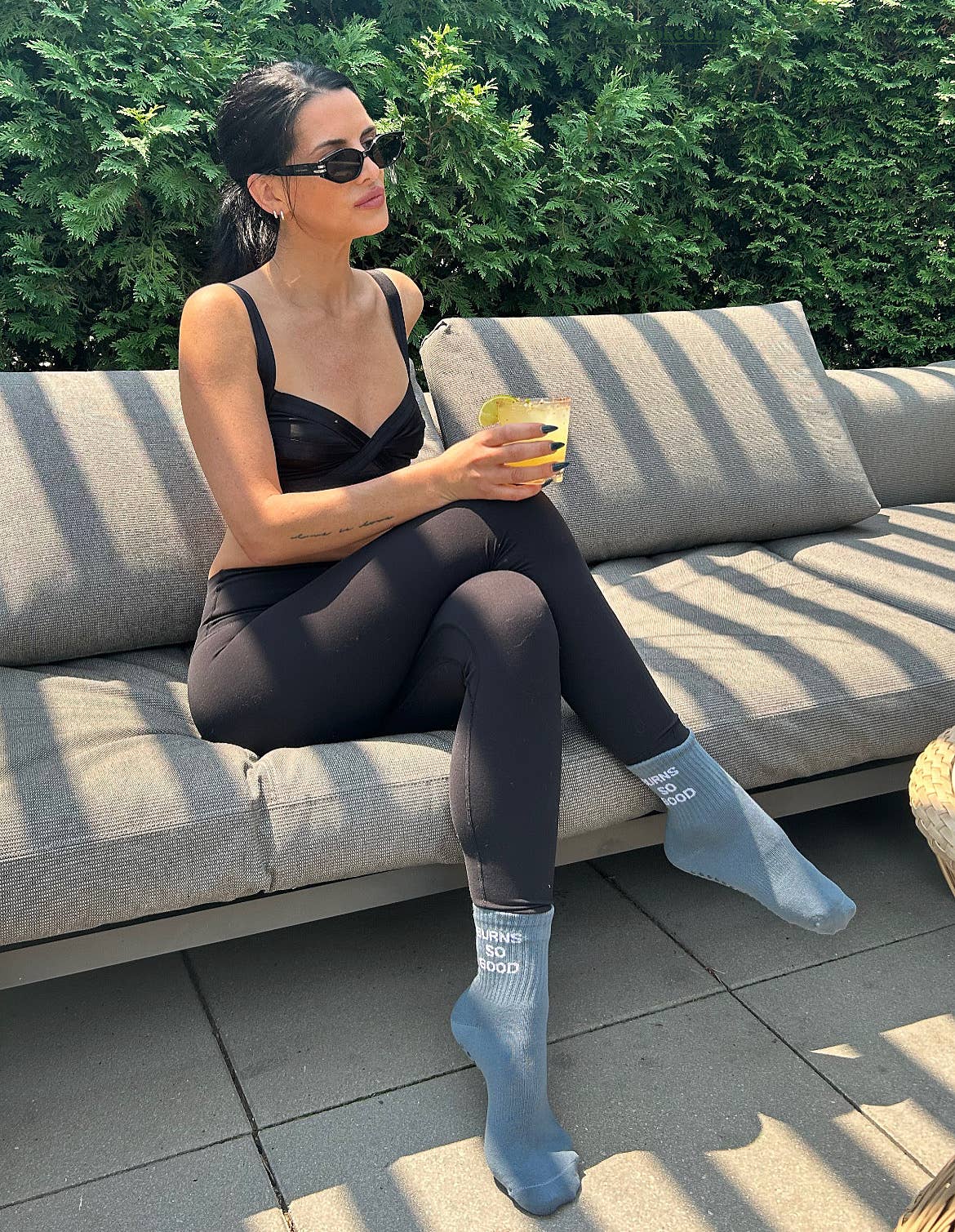 Woman relaxing outdoors in activewear while wearing blue BURNS SO GOOD grip socks with non-slip grips.