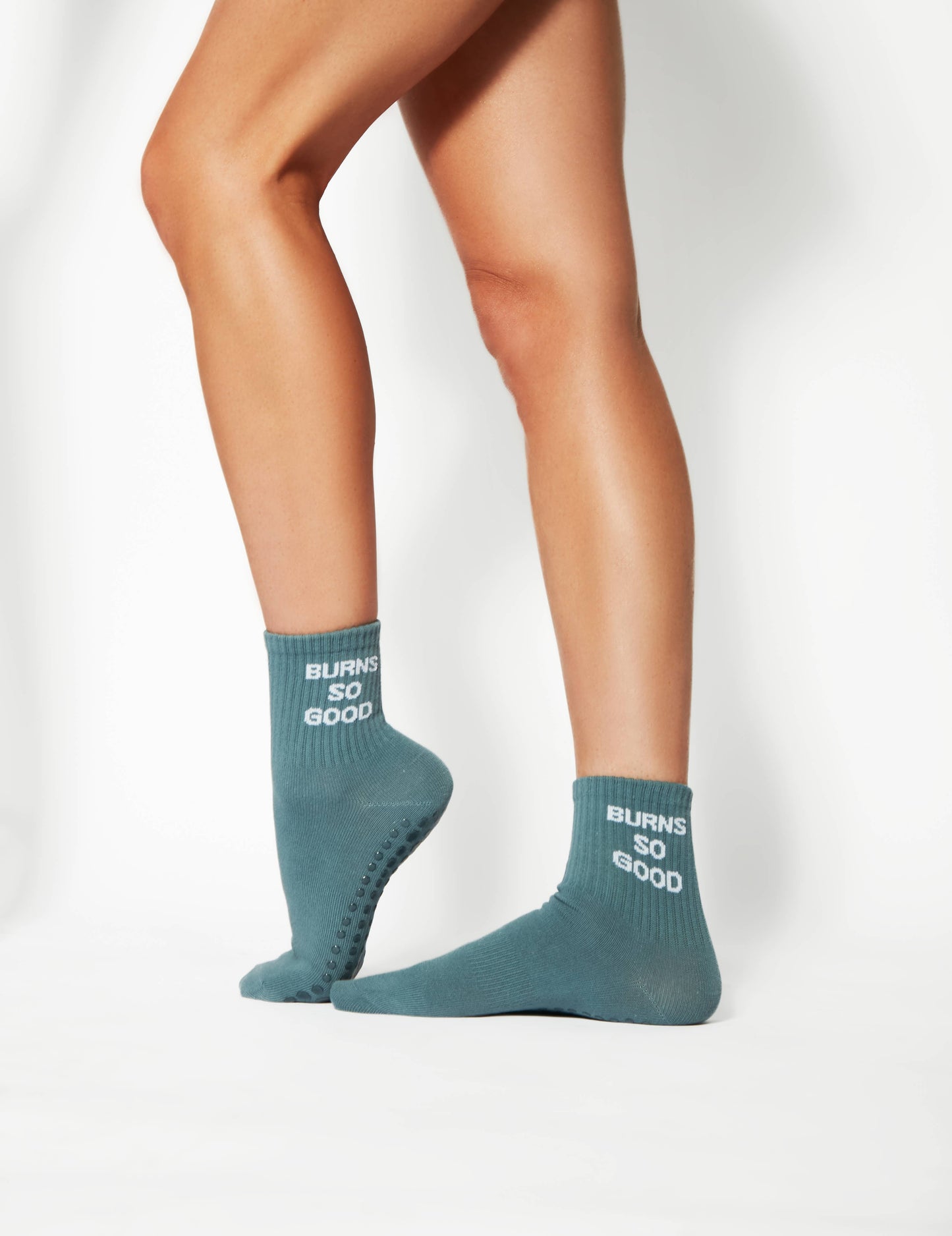 Close-up of blue BURNS SO GOOD grip socks showing ribbed cuffs, slogan detail, and non-slip grip dots on the sole.