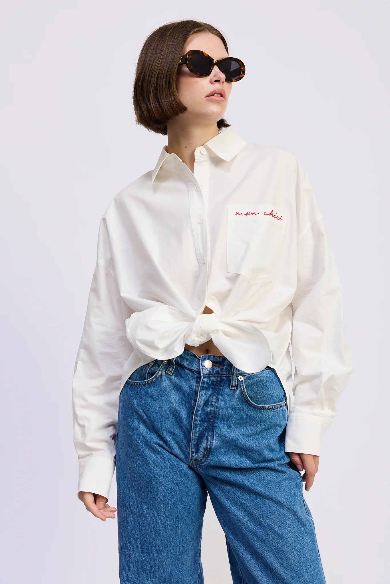 Model styling the Brittany Oversized Shirt tied at the waist with blue denim jeans and sunglasses