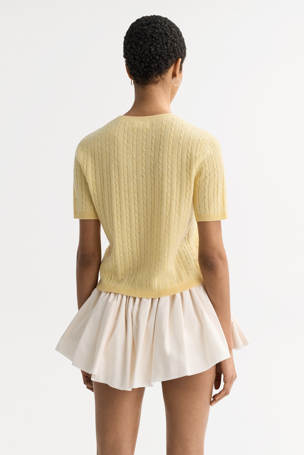 Model wearing the honeydew yellow cable knit cashmere top from the back with short sleeves and ribbed trim