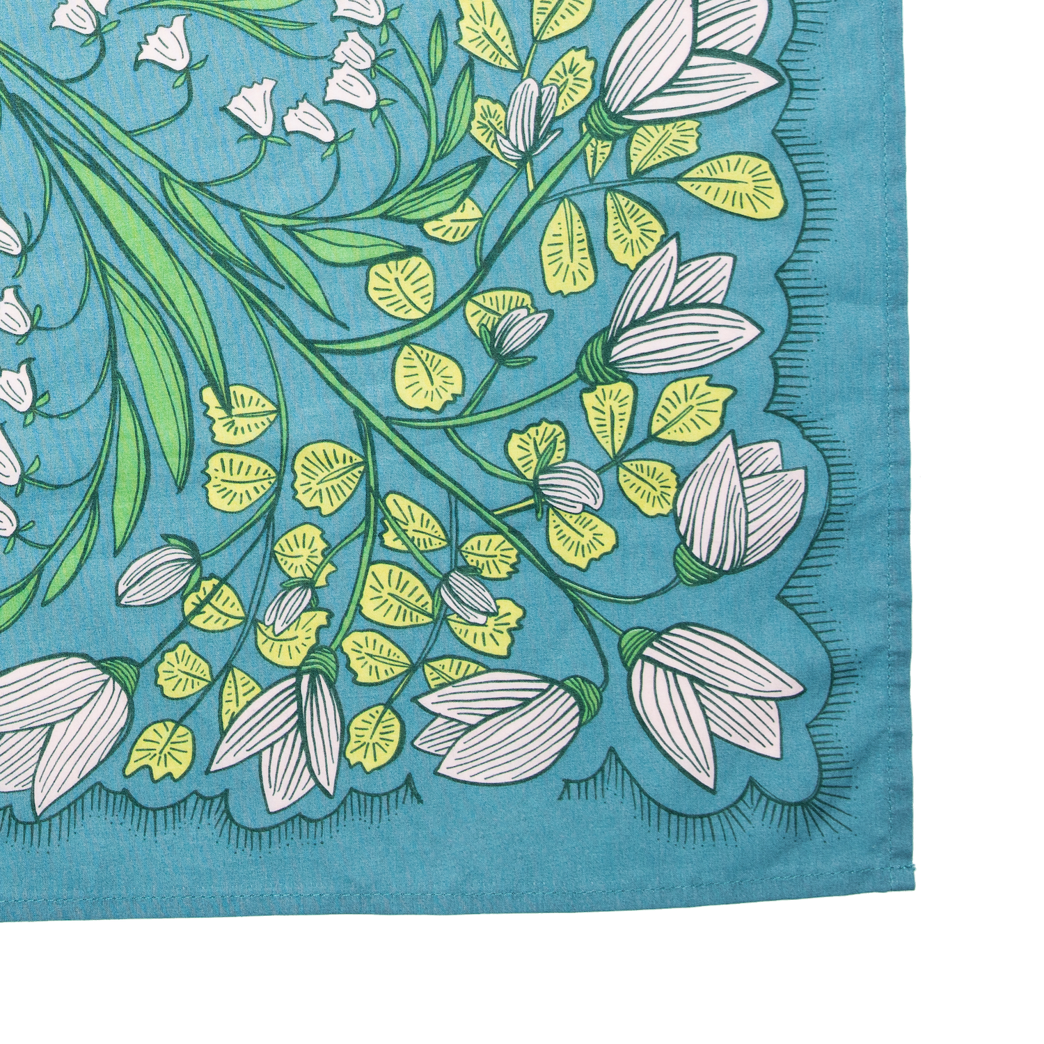 Close-up detail of the Cassie bandana showing the teal cotton fabric, white floral print, green leaves, and stitched edge.