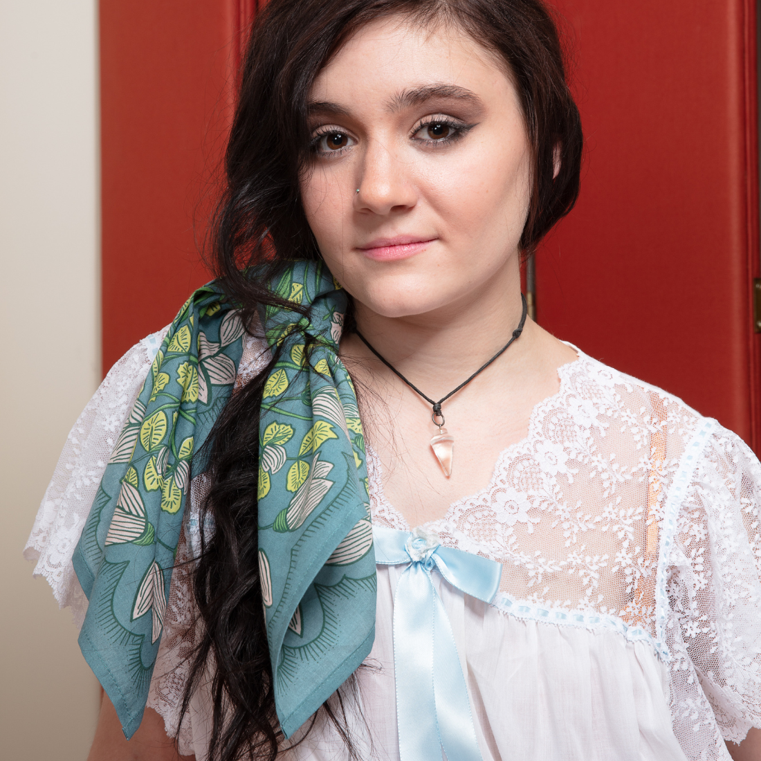 Cassie teal floral bandana styled over the shoulder with a white lace blouse for a soft, feminine accessory look.