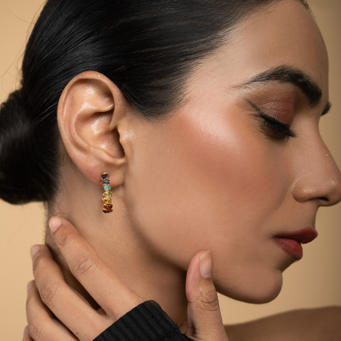 Model wearing gold-plated chakra hoop earrings with colorful natural stone accents.